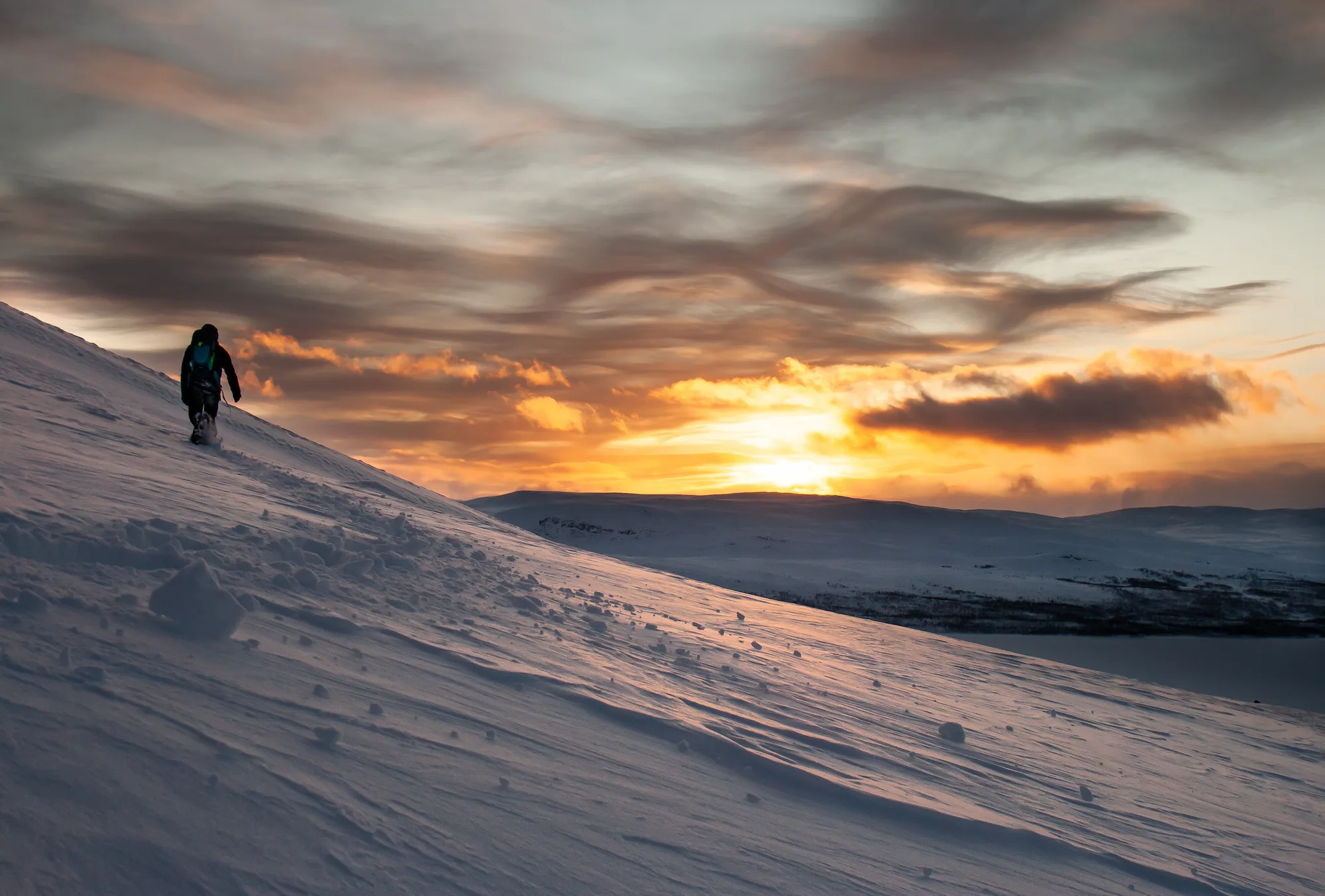 Une personne en raquettes montant un fell au-dessus des paysages d’Ylläs, au coucher du soleil